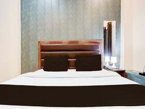 Ein Hotelzimmer mit einem großen Bett, zwei Kissen, einem Nachttisch mit Lampe und einem Fenster mit Vorhängen.