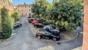 A parking area with multiple cars, a building with a tiled roof, and dense greenery. - Living 68 (Forlì)
