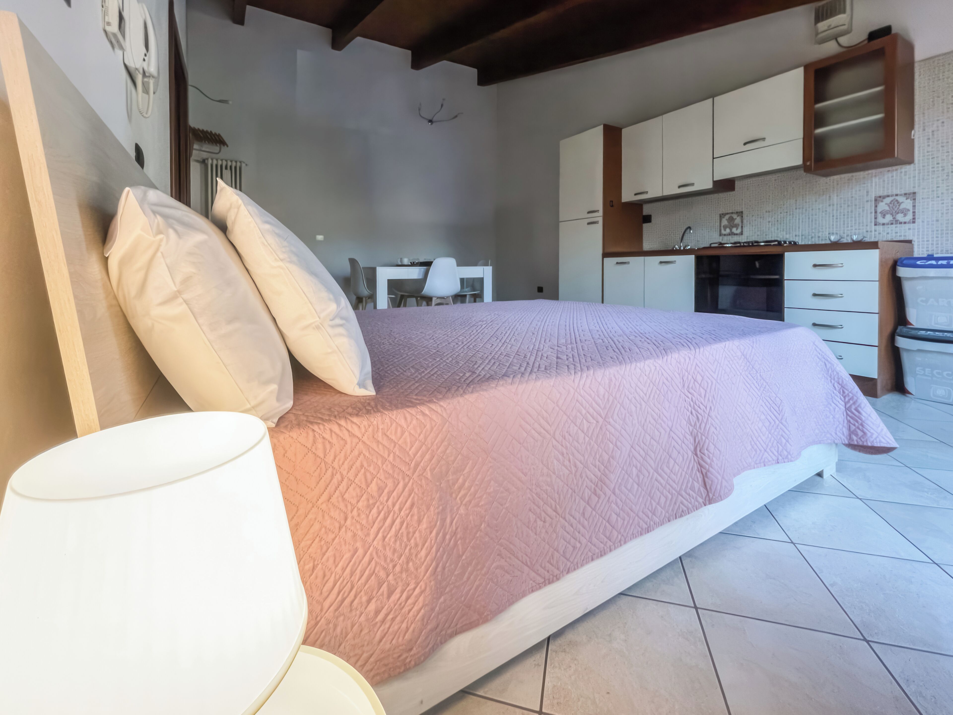 Un dormitorio con cama, almohadas, una mesita de noche y una lámpara.
