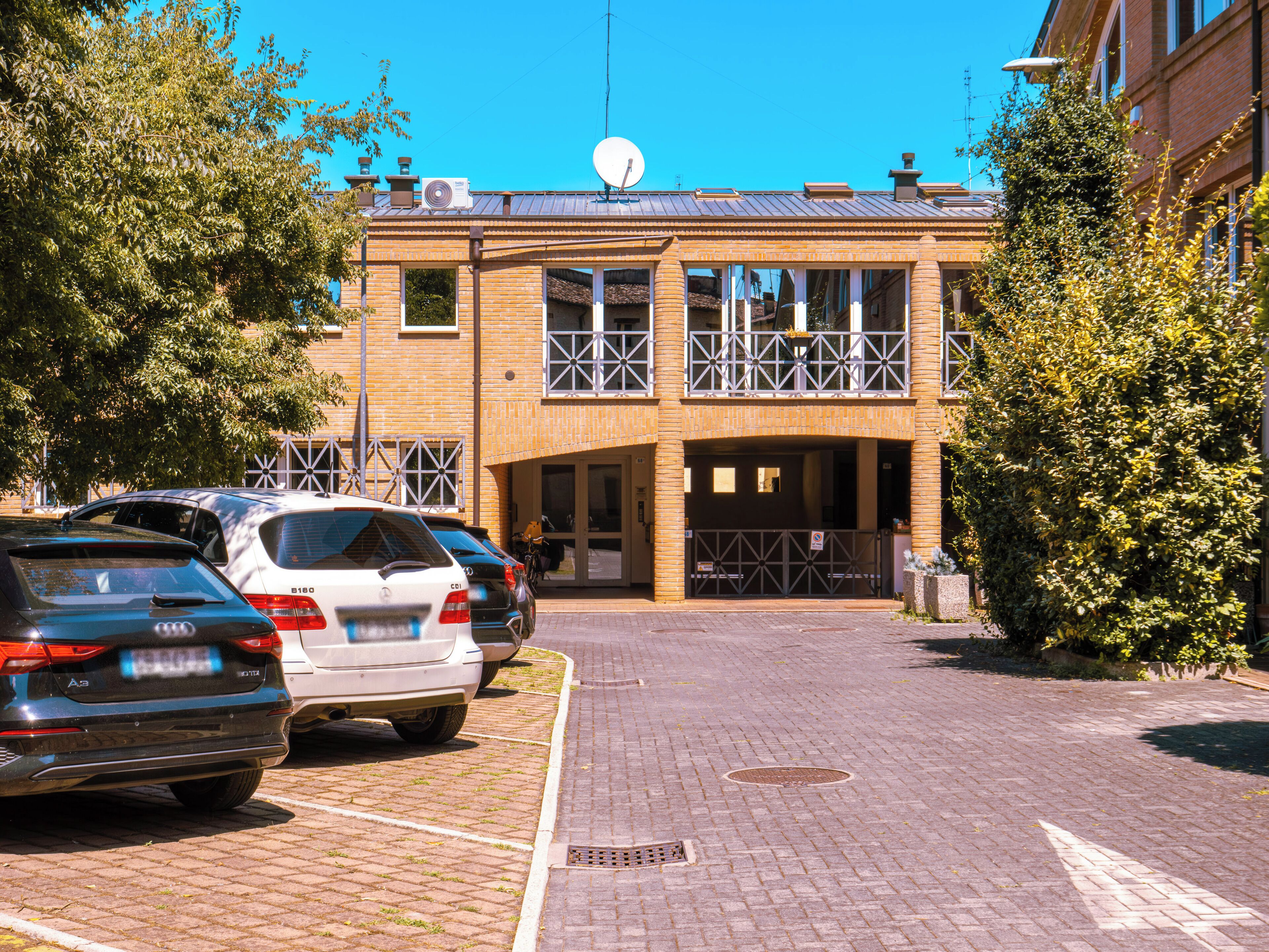 A parking lot with cars, a building with a satellite dish, and a gated entrance.