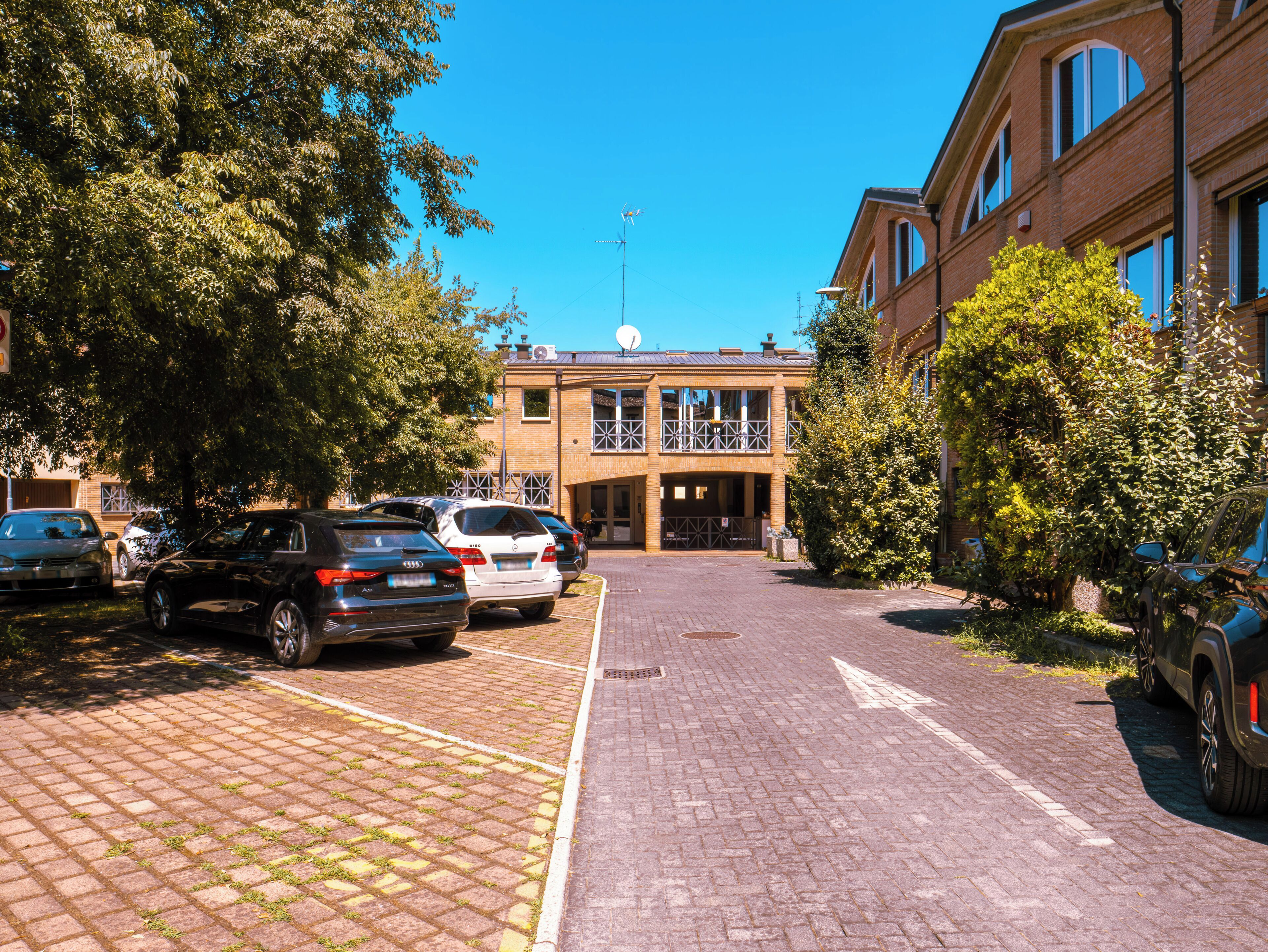 Un estacionamiento con varios autos, un edificio con balcón y árboles.