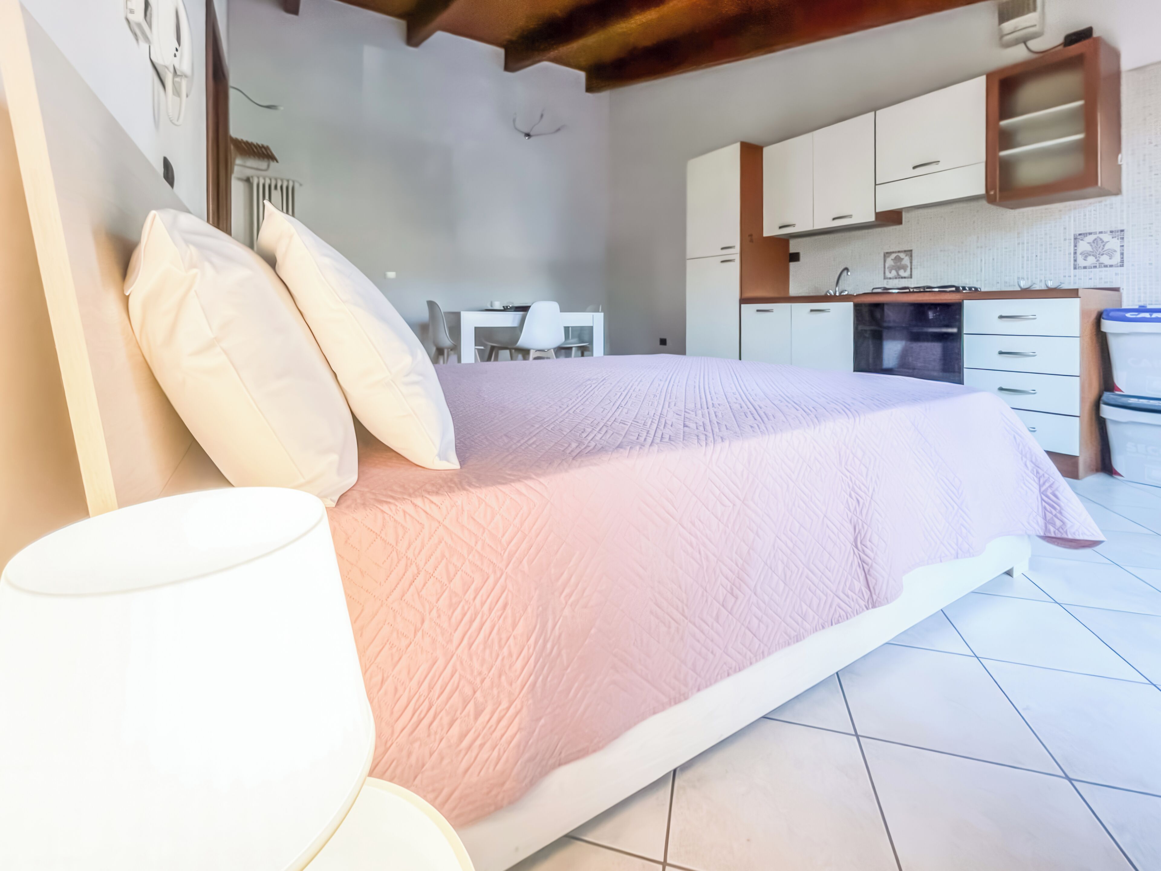 Un dormitorio con cama, almohadas, una mesita de noche y una lámpara.