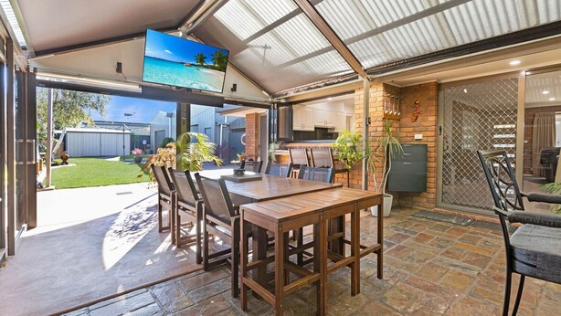 An outdoor patio with a wooden table and chairs, a TV screen, and a brick wall. - Maffra Retreat: Kick back and enjoy country Gippsland (Maffra)