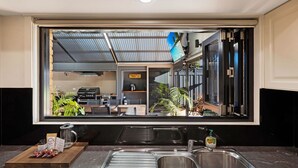A kitchen with a large mirror reflecting the interior, a sink, and a countertop with a cutting board and packaged food items. - Maffra Retreat: Kick back and enjoy country Gippsland (Maffra)
