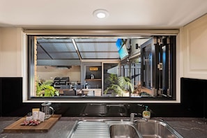 A kitchen with a large mirror reflecting the interior, a sink, and a countertop with a cutting board and packaged food items.