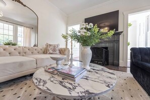 Ein Wohnzimmer mit einem beigen Sofa, einem runden Marmor-Couchtisch und einem Kamin.