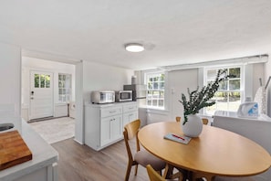 A modern kitchen with white cabinetry, a microwave, and a toaster. There is a dining table with chairs and a vase with a plant. - White Modern Retreat | Near Fort Moore & Downtown (Columbus)