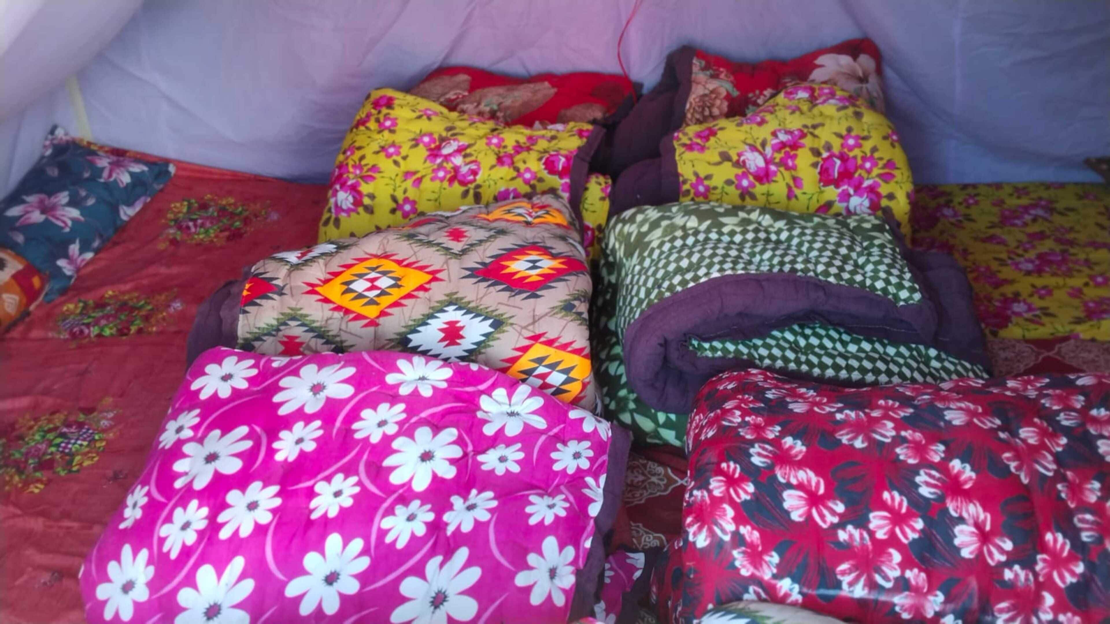 Una cama con varias almohadas y una manta, una almohada con diseño geométrico y una almohada estampada con motivos florales.