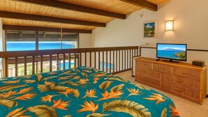 Ein Schlafzimmer mit Balkon, einem Bett mit tropischem Muster, einem Fernseher auf einer Holzkommode und Blick aufs Meer.
