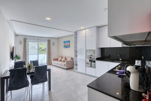 A modern kitchen with white cabinets, a black countertop, and a dining area with a table and chairs. - Modern 2 bedroom apartment, 2 balconies BZAR1-1 (St. Paul’s Bay)