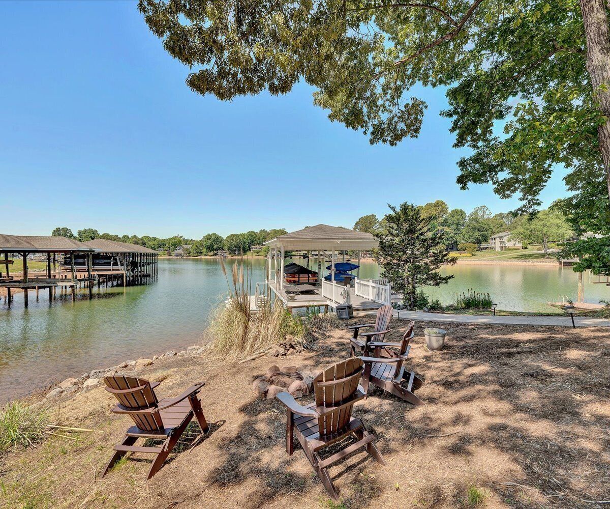 A lakeside deck with Adirondack chairs, a gazebo, and a dock extending into the water.
