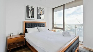 Una camera da letto moderna con un letto grande, un comodino in legno, una tavola da notte e due opere d'arte incorniciate al muro.