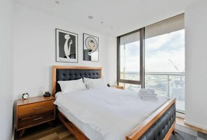 Ein modernes Schlafzimmer mit einem großen Bett, einem Nachttisch aus Holz, einer Nachttischlampe und zwei gerahmten Kunstwerken an der Wand.