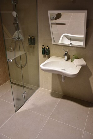 Une salle de bain moderne avec une douche à parois de verre, un lavabo blanc et un miroir qui reflète le lavabo et la douche.