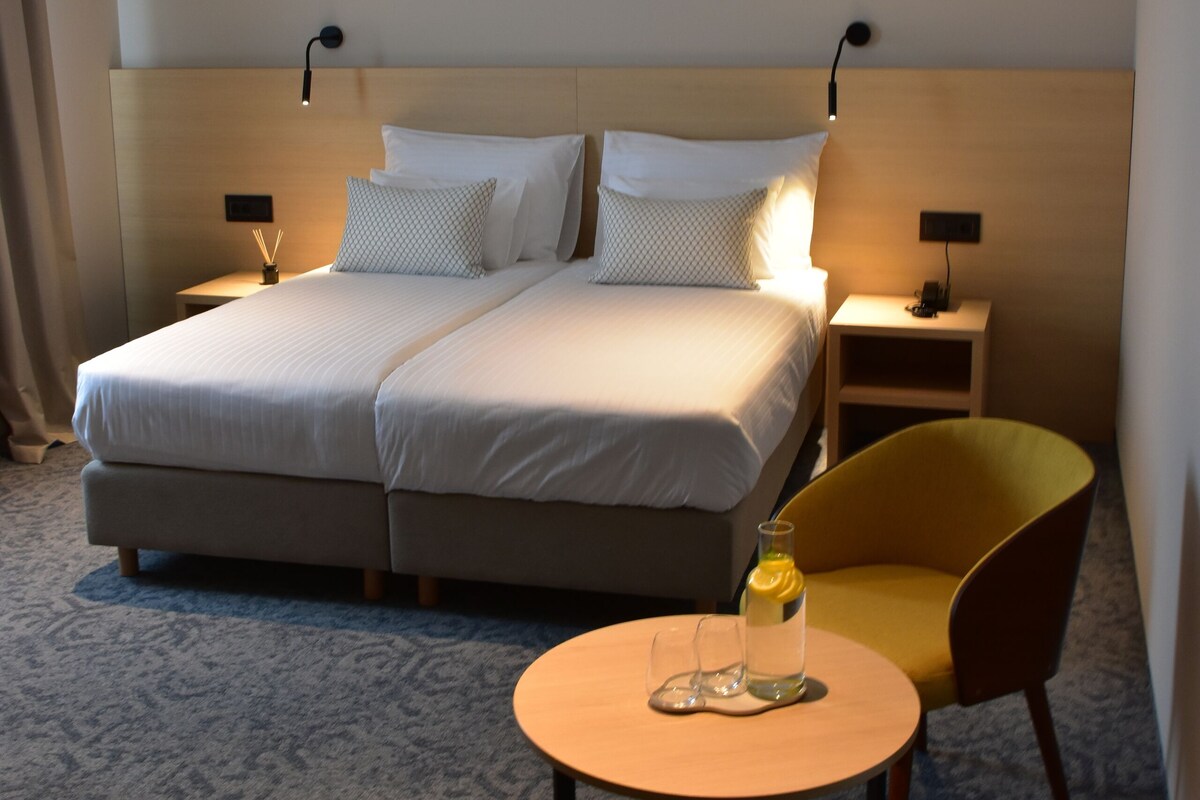 Una habitación de hotel con una cama grande, mesitas de noche, una silla y una pequeña mesa.