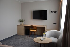 Habitación de hotel con escritorio, una silla, televisor montado en la pared, una mesita con un vaso y una planta en maceta.
