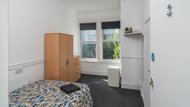 A room with a bed, wardrobe, radiator, windows, and a door with a number. - Room 3 - The Archers (Southampton)