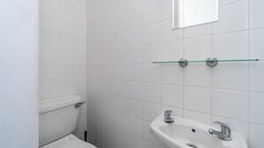A bathroom with white tiles, a toilet, a sink, and a glass shelf. - Room 3 - The Archers (Southampton)