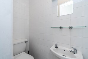 Ein Badezimmer mit weißen Fliesen, einer Toilette, einem Waschbecken und einer Glasablage.