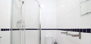 A bathroom with white tiles, a glass shower enclosure, a toilet, and a grab bar. - Pebbles Guest House - Flat 1 (Southampton)