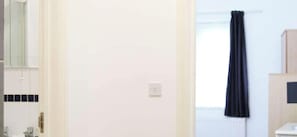 A bathroom with a white door, a window with a black curtain, and a radiator. - Pebbles Guest House - Flat 1 (Southampton)