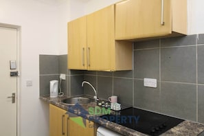 A small kitchen with a sink, countertop, and wooden cabinets. - Pebbles Guest House - Flat 1 (Southampton)