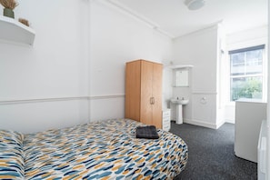 Ein Schlafzimmer mit Bett, Schrank, Waschbecken und Fenster.