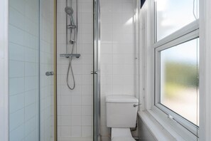 Ein kleiner, abgeschlossener Duschbereich mit Glastür, Toilette und einem Fenster mit Milchglas.