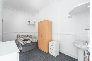 Ein Schlafzimmer mit Bett, Kleiderschrank, Nachttisch und einem Badezimmer inklusive Waschbecken und Spiegel.