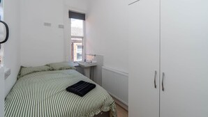 Un dormitorio con cama, ventana, radiador y armario.