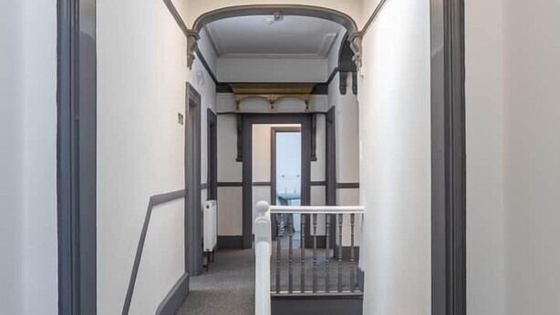 Una escalera con tragaluz, peldaños alfombrados y barandilla blanca.