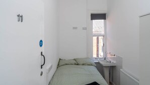 Una habitación pequeña y estrecha con una cama, un ventanal, un radiador y un lavamanos.