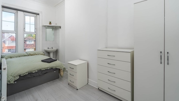 Un dormitorio con cama, mesita de noche, armario, espejo y ventana.
