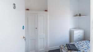 Ein Schlafzimmer mit Bett, einem weißen Kleiderschrank, einer Tür und einem Regal mit einer Pflanze.