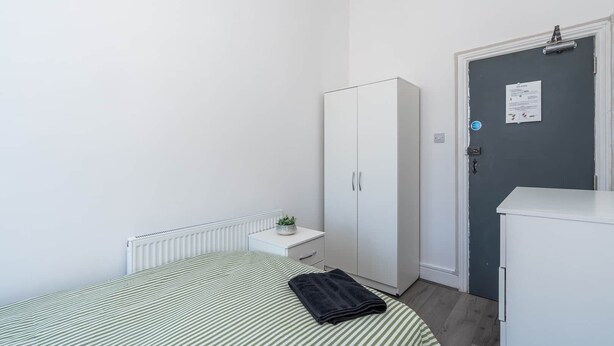Une chambre à coucher comprenant un lit, une armoire, un radiateur et une porte sur laquelle est affiché un avis.