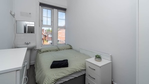 Une petite pièce propre, avec un lit, une table de chevet, un radiateur, une fenêtre et un miroir.