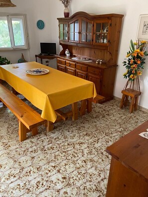Ein Essbereich mit einem langen Holztisch, der mit einer gelben Tischdecke bedeckt ist, einer hölzernen Bank, einem Schrank mit Glastüren und einer Blumenkomposition.