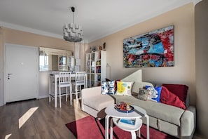 A modern living room with a sofa, a small table, and a dining area with chairs. - Magnifique appartement climatisé vue mer (Toulon)