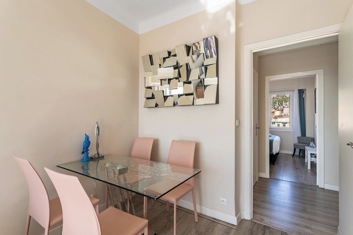 A dining area with a glass table and pink chairs, a wall art piece, and a view into another room.