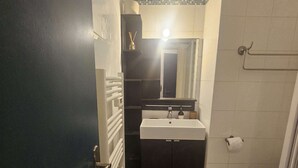 Une salle de bain avec un lavabo blanc, des meubles sombres, un miroir, un porte-serviettes et des toilettes.