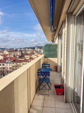 Un balcone con vista sulla città, un tavolo e sedie, e un vaso rosso.