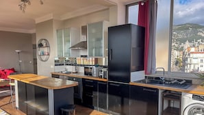 Une cuisine moderne dotée d’un îlot central, d’appareils électroménagers intégrés et offrant une vue sur le paysage urbain.
