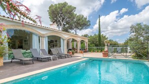 Ein Schwimmbad mit Liegestühlen, einer überdachten Terrasse und Topfpflanzen.