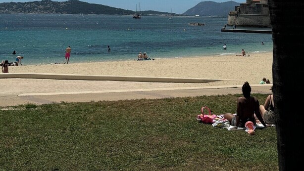 A beach with clear skies, calm sea, and a distant hill.