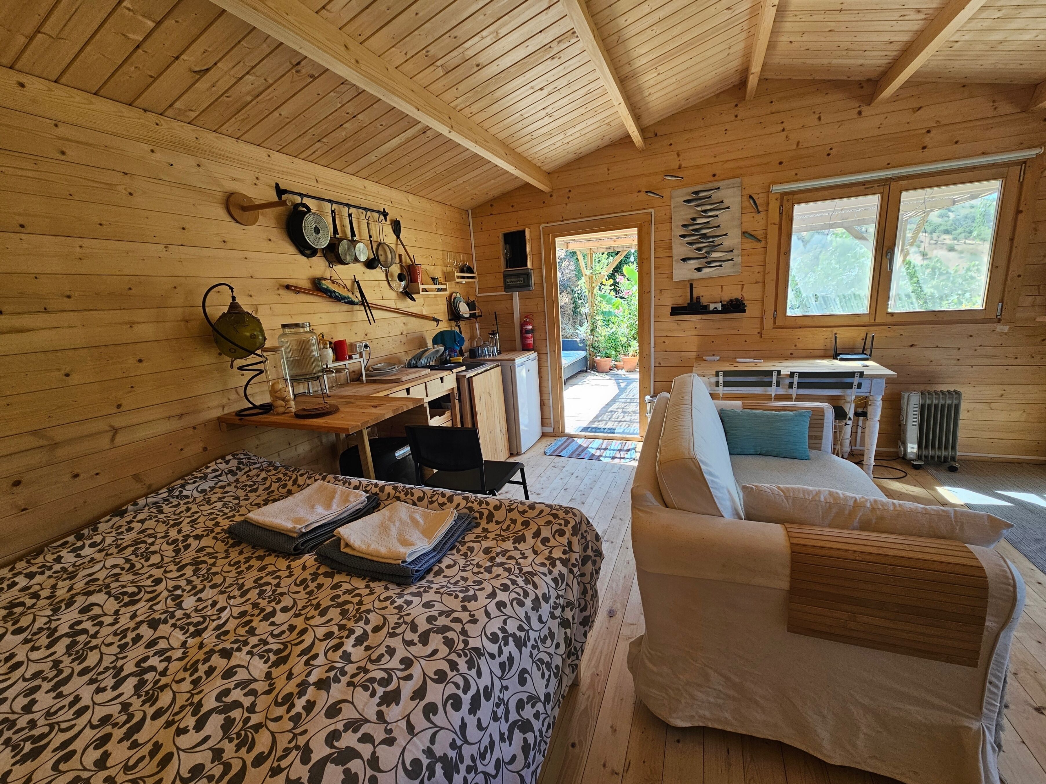 A wooden cabin interior with a dining area, a sofa, and a bed.