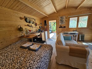 Interior de una cabaña de madera con comedor, sofá y cama.