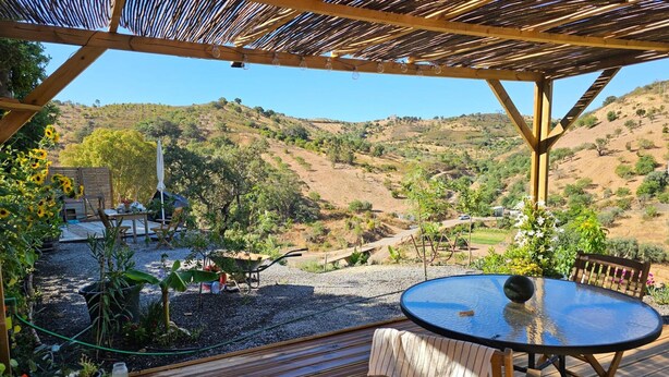 A wooden deck with a table and chairs, overlooking a hilly landscape. - Cabin Sleeps 2 With Enclosed Garden (Tavira)