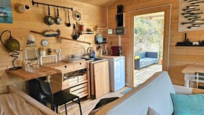 A compact, wooden cabin with a kitchenette, a dining area, and a sofa. - Cabin Sleeps 2 With Enclosed Garden (Tavira)