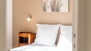 A bedroom with a bed, pillows, a nightstand, a wall-mounted light, and two paintings of a beach scene. - Les Sablettes Jardin & Parking 5 min de la Plage (La Seyne-sur-Mer)