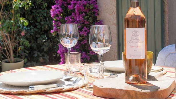A table set outdoors with a bottle of wine, glasses, and plates, surrounded by purple flowers and a green door. - Les Sablettes Jardin & Parking 5 min de la Plage (La Seyne-sur-Mer)
